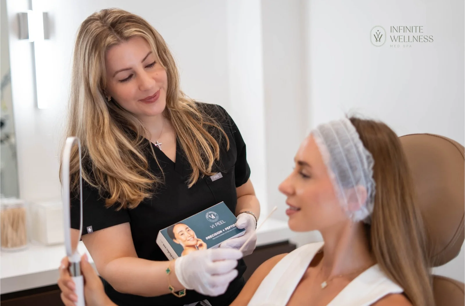 An aesthetician at Infinite Wellness Med Spa shows a VI Peel kit to a client during a consultation.