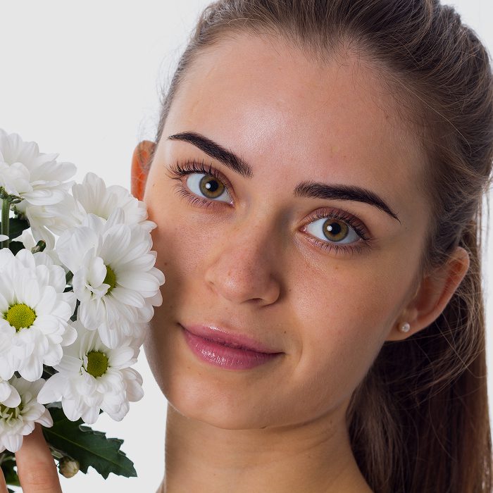 Close-up portrait of a smiling woman with a bouquet of white daisies beside her face on the left side.